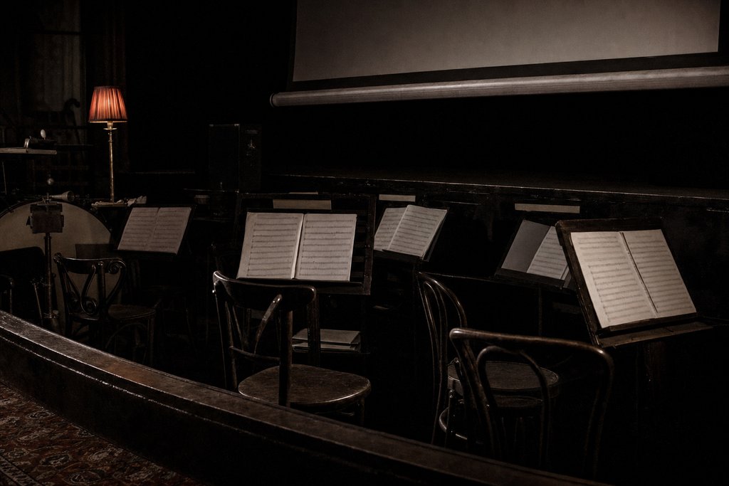 An empty orchestra pit in a small picture house, music stands still carrying parts.