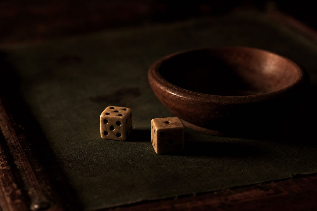 A pair of dice at rest on worn dark green baize beside a shallow wooden bowl