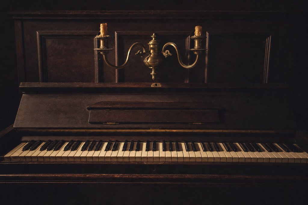 A piano keyboard with the fallboard open, a brass candle sconce above the keys.