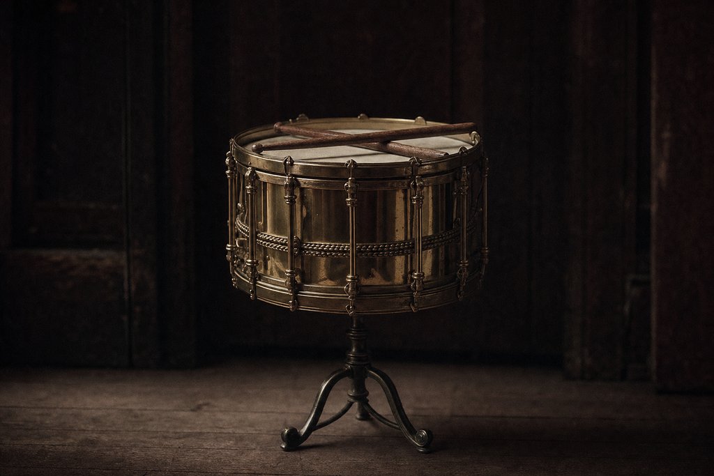 A brass military side drum on a stand, a pair of sticks resting across the head.