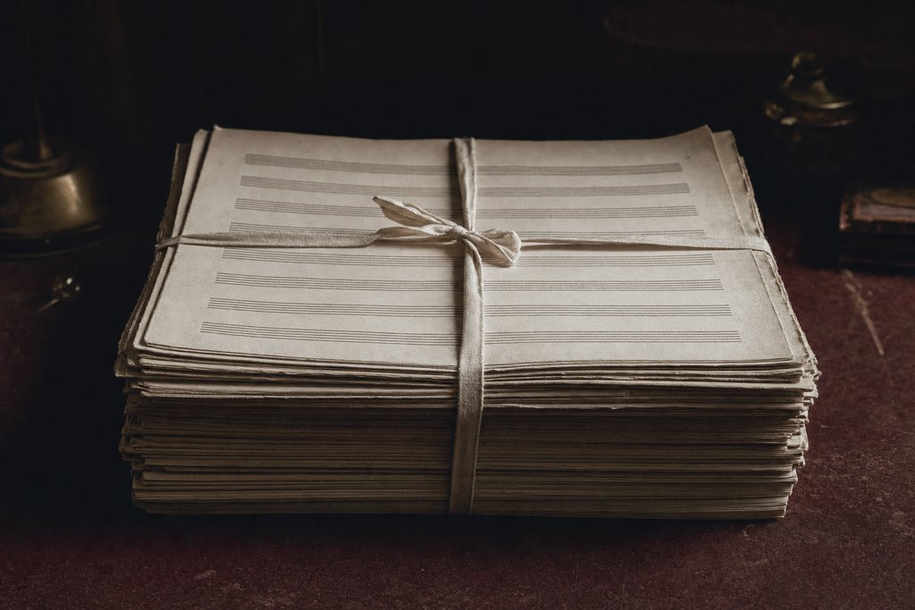 A thick stack of orchestral parts tied with cotton tape, the top sheet ruled with empty staves.