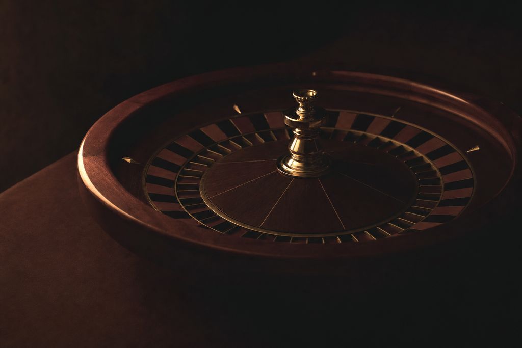 A roulette wheel at rest on a dark table, lit from one side, the pockets falling away into shadow