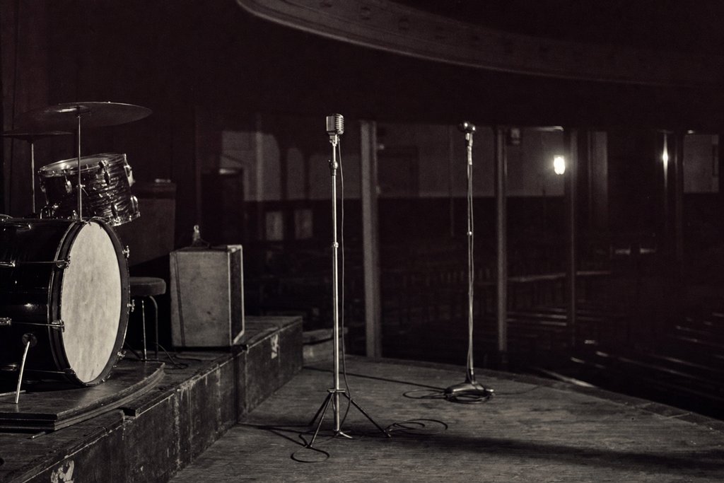 A small venue stage before the doors open: two microphones, a drum riser, coiled cables.