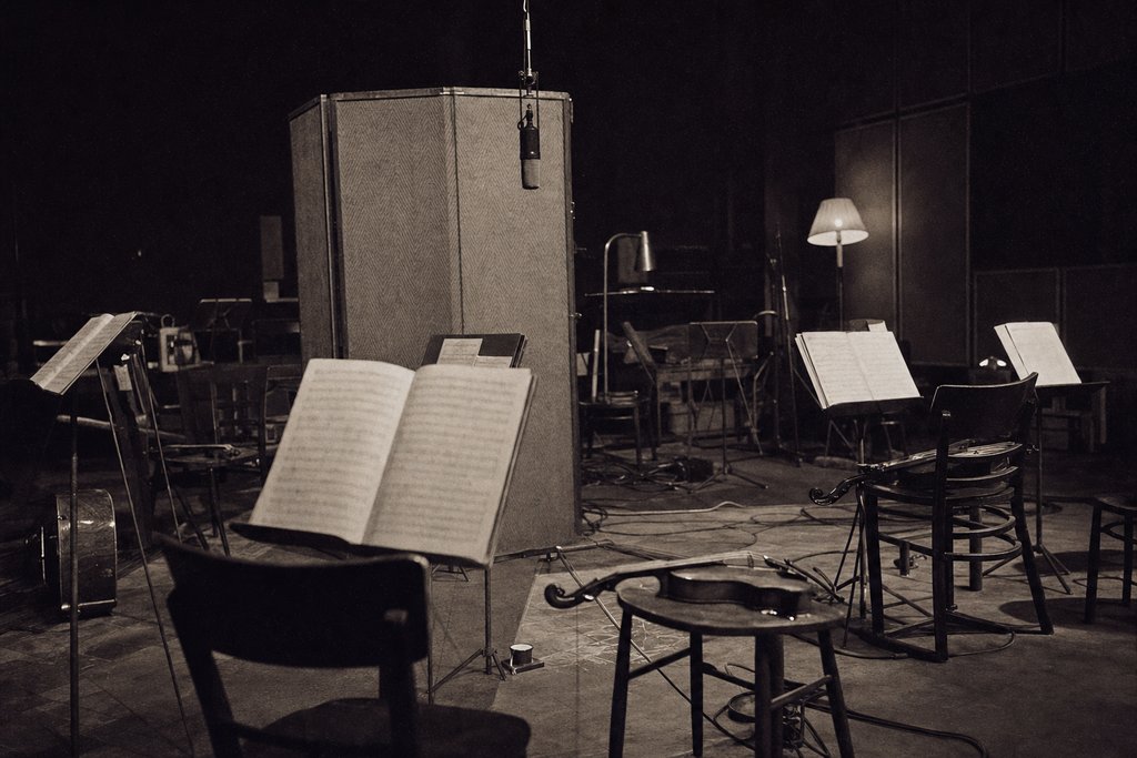 A radio studio floor photographed from behind an empty string section, parts open on the stands.